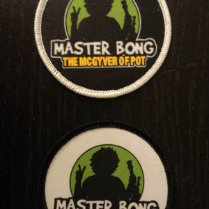 Peut inclure: Deux patchs ronds noirs et blancs avec un cercle vert au centre. Le cercle repr&eacute;sente une silhouette d'une personne tenant un bang. Le texte "Master Bong The McGyver of Pot" est imprim&eacute; en jaune sur les patchs.
