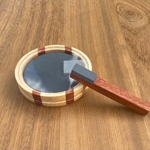 May include: A wooden ring with a dark gray center and red and white stripes. A wooden stick with a gray top is next to the ring.