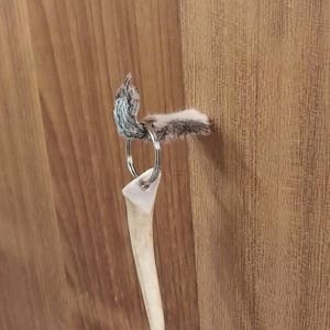 May include: A handmade keychain featuring a natural antler pendant. The keychain includes a silver-colored split ring and is adorned with a small piece of fur. The antler pendant is a light beige color.