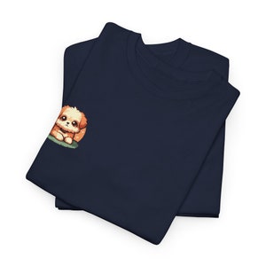 May include: A navy blue t-shirt is folded in half.  A small, cartoon illustration of a fluffy, light brown dog is embroidered on the left chest area. The dog is sitting and looking to the right. The t-shirt is made of a soft, comfortable fabric and is perfect for everyday wear. The folded t-shirt shows the neckline and the overall shape of the garment. The image shows two shirts stacked on top of each other.