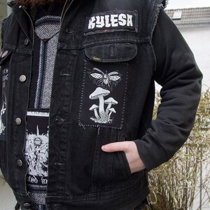 May include: A black denim vest featuring a rectangular patch with a white graphic of mushrooms and a winged insect. The vest includes a rectangular patch with the text Kylesa and another patch with a detailed black and white illustration.
