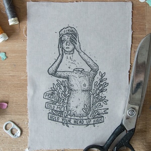 Puede incluir: Una ilustración en blanco y negro de una persona con la cabeza cubierta por sus manos. La ilustración está impresa en una tela beige con el texto "Mama told me hold your head up high".
