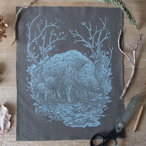 Pode incluir: Um remendo de tecido azul e cinza com um desenho de um javali selvagem e seus filhotes em um ambiente de floresta. O javali e seus filhotes são cercados por árvores e cogumelos.