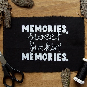 Op de afbeelding: Zwarte stof met witte tekst "Memories, sweet fuckin' Memories."