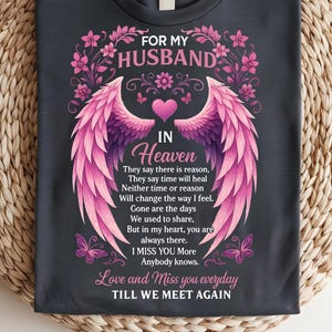 Może przedstawiać: Ciemnoszara koszulka z różowym kwiatowym i anielskim skrzydłem. Tekst brzmi "FOR MY HUSBAND IN HEAVEN" z wierszem o tęsknocie za ukochaną osobą. Zawiera serca i motyle.