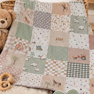 Könnte beinhalten: Eine Patchwork-Babydecke mit einem Bauernhof-Motiv, das Illustrationen von Pferden, Schafen, Traktoren, Scheunen, Bäumen und Zäunen in gedeckten Erdtönen wie Salbeigrün, Beige und Weiß zeigt, ergänzt durch einen braunen Teddybären und einen Holzring.