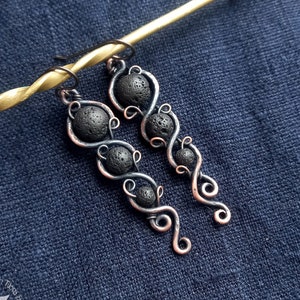 Könnte beinhalten: Ein Paar lange, baumelnde Ohrringe mit schwarzen Lavasteinen und silbernem Draht, der in einem wirbelnden Design umwickelt ist.