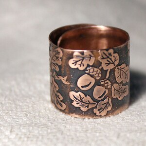 Puede incluir: Un anillo de cobre con un dise&ntilde;o de hojas y bellotas. El anillo est&aacute; hecho de cobre martillado y tiene un aspecto r&uacute;stico.