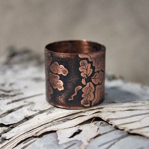 Puede incluir: Un anillo de cobre con una p&aacute;tina marr&oacute;n oscura y un dise&ntilde;o grabado de hojas de roble.