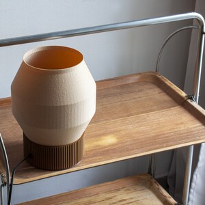 May include: A beige ceramic lamp with a brown base sits on a wooden shelf of a metal rolling cart.