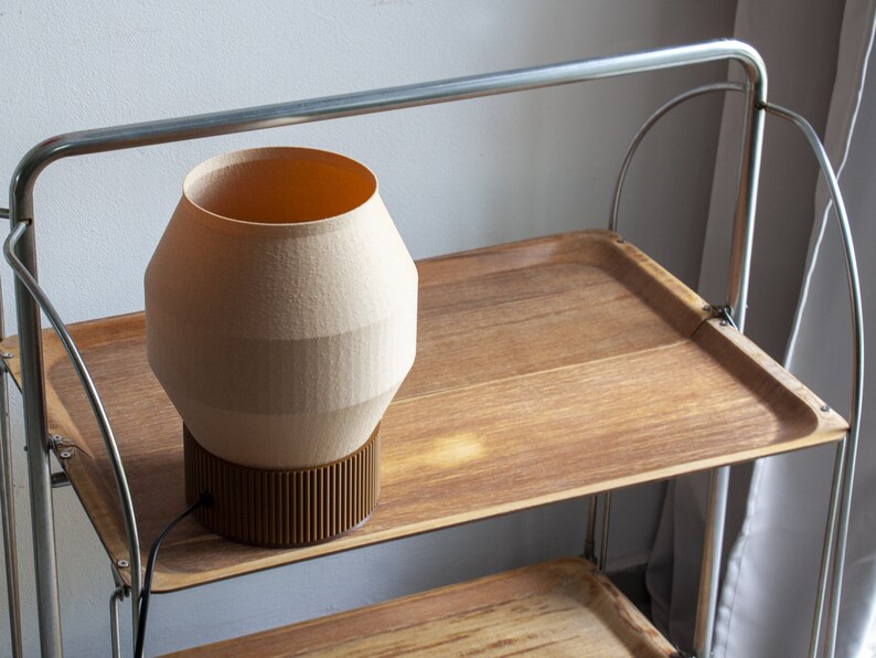 May include: A beige ceramic lamp with a brown base sits on a wooden shelf of a metal rolling cart.