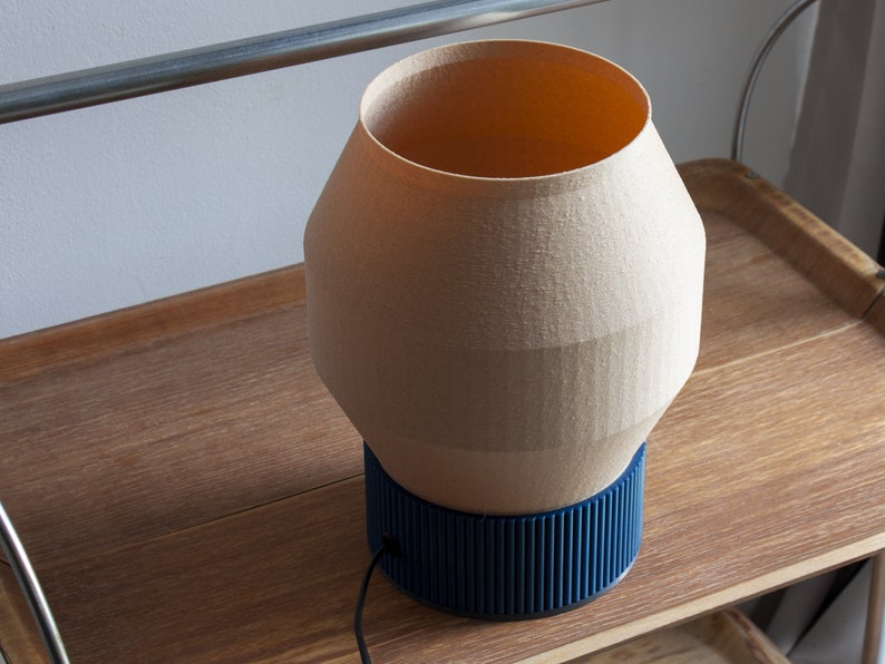 May include: A beige ceramic table lamp with a blue ribbed base. The lamp is sitting on a wooden surface.