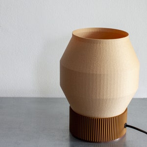 May include: A beige table lamp with a geometric, rounded shade and a brown, ribbed base. The lamp has a black cord.
