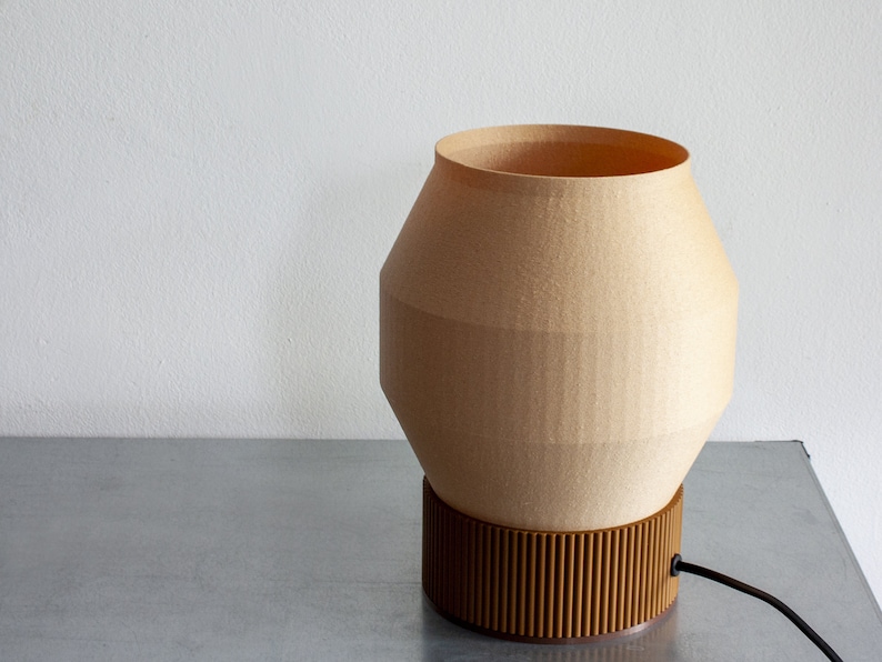 May include: A beige table lamp with a geometric, rounded shade and a brown, ribbed base. The lamp has a black cord.