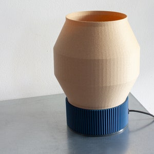 May include: A beige table lamp with a blue base. The lamp has a geometric shape and a cord.