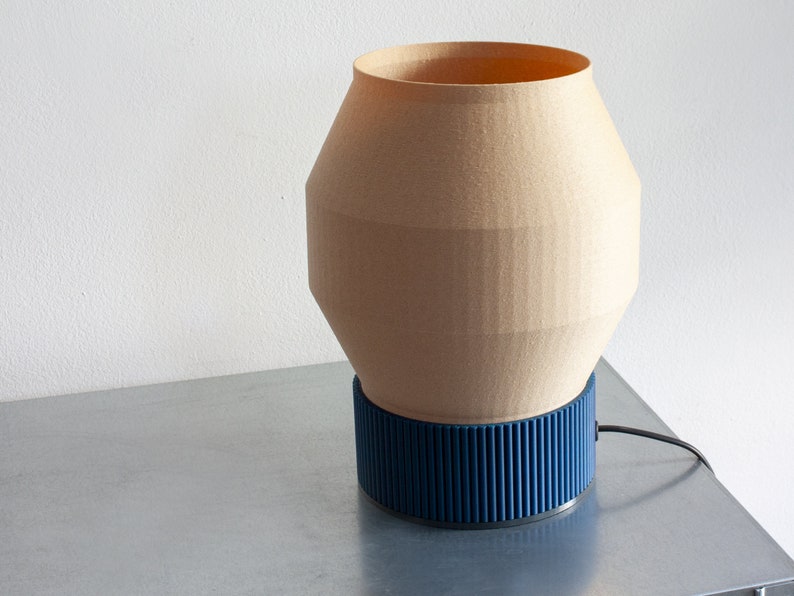 May include: A beige table lamp with a blue base. The lamp has a geometric shape and a cord.