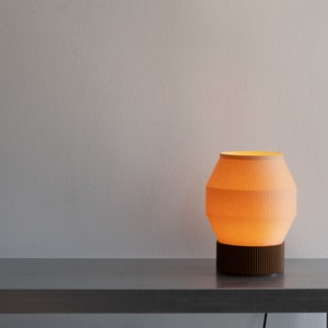May include: A modern table lamp with a light orange fabric shade and a dark brown wooden base. The lamp is on a silver metal table.