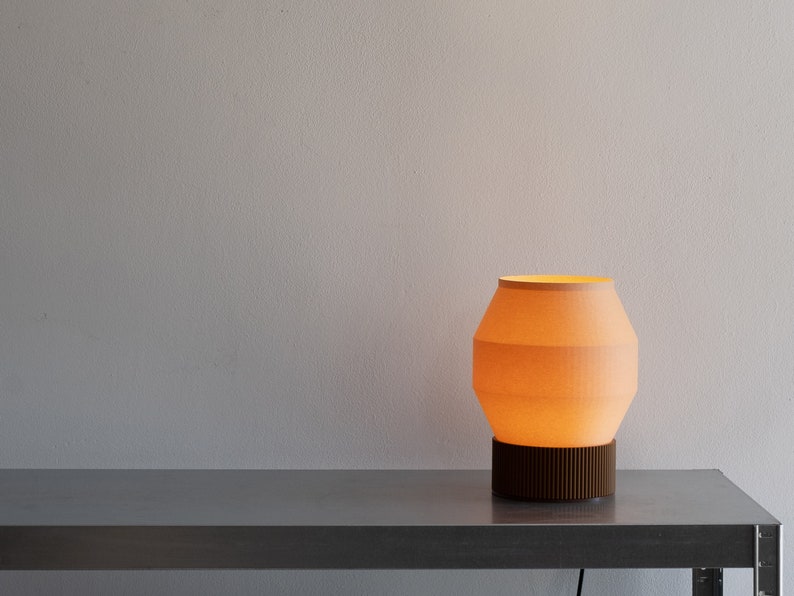 May include: A modern table lamp with a light orange fabric shade and a dark brown wooden base. The lamp is on a silver metal table.