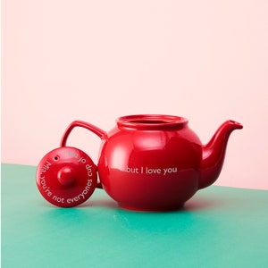 May include: Red ceramic teapot with a lid that reads "You're not everyone's cup of tea, but I love you".