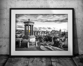 May include: A black and white photograph of a cityscape with a monument in the foreground. The monument is a tall, round structure with columns and a dome. The city is in the background and is made up of buildings, trees, and a river. The photograph is framed in a black frame.
