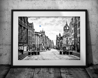 May include: A black and white photograph of a street in Edinburgh, Scotland. The street is lined with buildings on both sides, and there is a Scottish flag flying from a building in the distance.