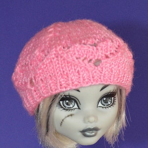 May include: A doll with pale grey skin and black eyeliner wearing a pink knitted beret and a black and white patterned dress.