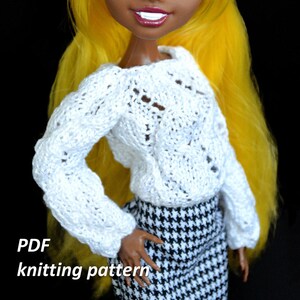May include: A white knitted sweater with a delicate pattern, worn by a doll with yellow hair and brown skin. The doll is wearing a black and white houndstooth skirt. The image includes the text "PDF knitting pattern".