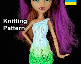May include: Knitting pattern for a doll's dress. The dress is white with a green ombre skirt. The doll has purple hair and green eyes.
