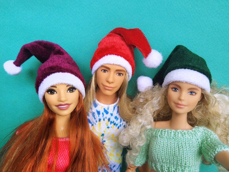 Puede incluir: Tres mu&ntilde;ecas con gorros de Pap&aacute; Noel. Las mu&ntilde;ecas llevan un gorro de Pap&aacute; Noel rojo, burdeos y verde. Las mu&ntilde;ecas tienen el pelo largo y miran a la c&aacute;mara.
