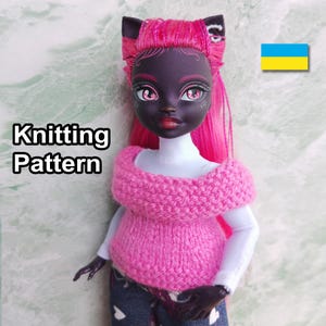 May include: A doll with dark skin, pink hair, and cat ears, wearing a knitted pink sweater. The text "Knitting Pattern" is displayed on the left. The doll is wearing a white shirt and blue jeans. A Ukrainian flag is in the background.