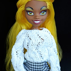 May include: A doll with yellow hair, brown skin, and bright makeup wearing a white knitted sweater and a black and white houndstooth skirt.