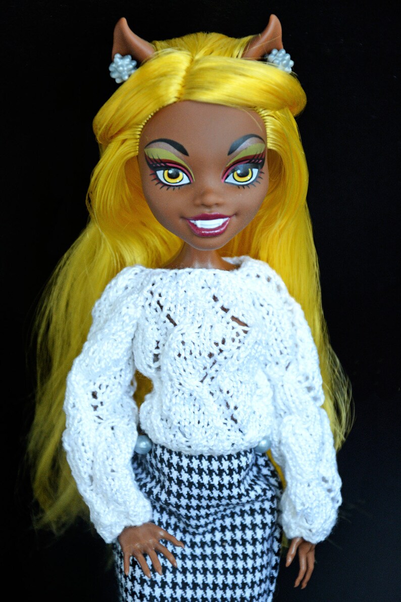 May include: A doll with yellow hair, brown skin, and bright makeup wearing a white knitted sweater and a black and white houndstooth skirt.