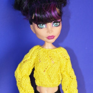 May include: A doll with black and purple hair wearing a yellow knitted sweater and black pants.