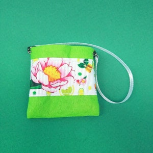 Puede incluir: Una peque&ntilde;a bolsa de fieltro verde con una cinta floral blanca y un asa de cinta blanca.