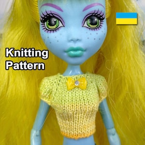 May include: Knitting pattern for a yellow and green ombre doll top with a yellow bow and a rhinestone. The pattern includes instructions for knitting a doll top with short sleeves. The doll is wearing the top and has blue skin, green eyes, and yellow hair. The text "Knitting Pattern" is visible in the image.