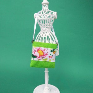 Puede incluir: Un maniqu&iacute; blanco con una bolsa de tela verde con estampado floral y ribete blanco. La bolsa tiene una correa blanca.