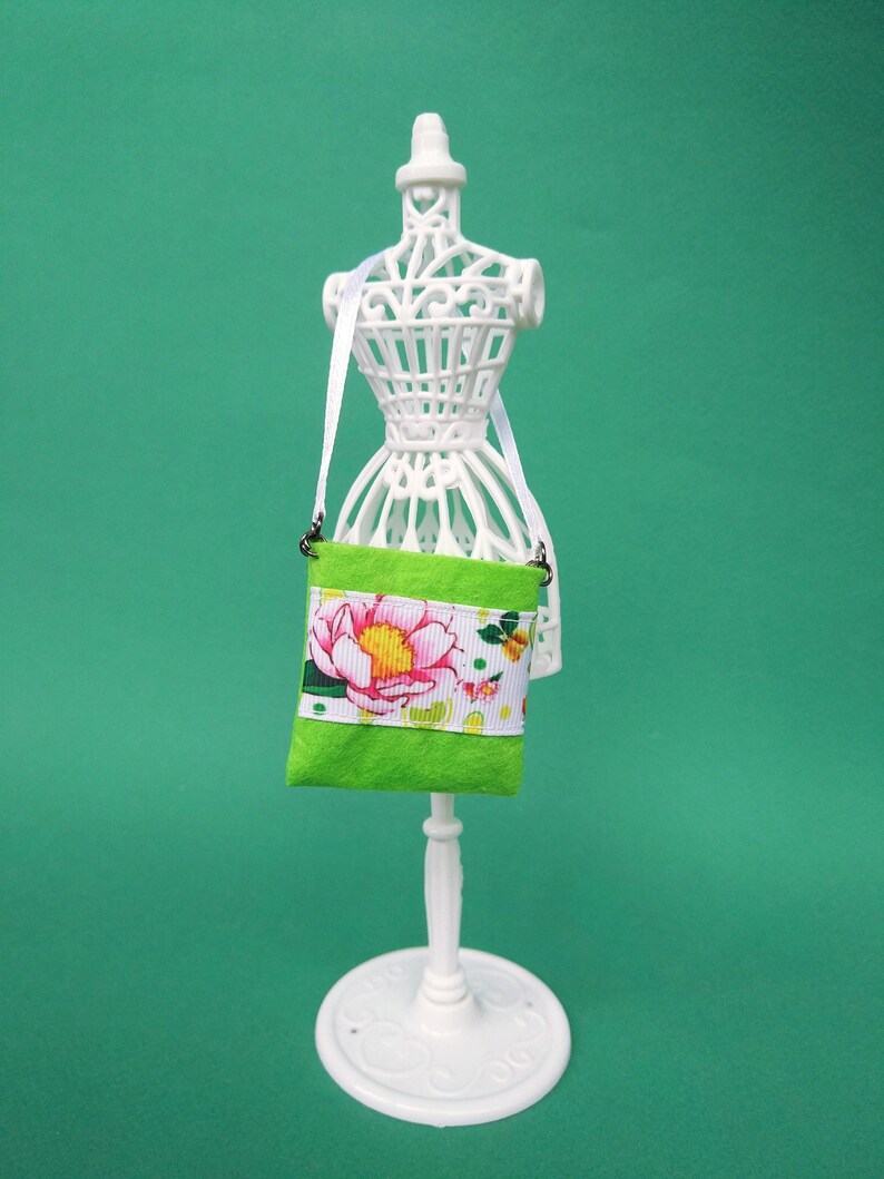 Puede incluir: Un maniqu&iacute; blanco con una bolsa de tela verde con estampado floral y ribete blanco. La bolsa tiene una correa blanca.