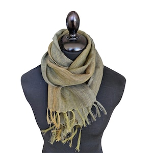 Peut inclure: Écharpe tissée vert olive et marron, présentée sur un mannequin noir. L'écharpe a une bordure à franges et un aspect texturé. L'écharpe est drapée autour du cou du mannequin.