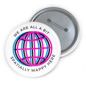 以下が含まれることがあります： 黒とピンクの地球儀のデザインと「We are all a bit spatially mappy here」というテキストが書かれた白いボタンです。