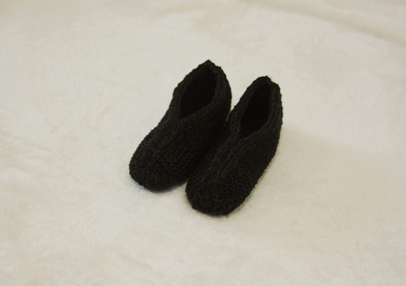 May include: A pair of black knitted slippers. The slippers are made of a soft, comfortable material and have a simple, classic design.