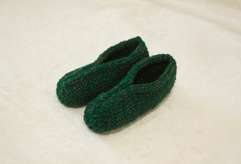 May include: A pair of green knitted slippers with a dark green pattern. The slippers are made of soft yarn and have a comfortable fit.