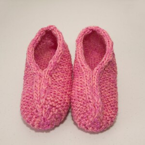 May include: A pair of pink knitted slippers with a cable knit design.
