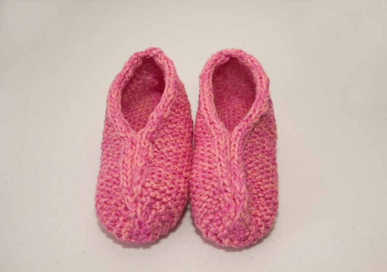 May include: A pair of pink knitted slippers with a cable knit design.