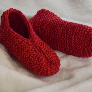 May include: A pair of red knitted slippers. The slippers are made with a soft, cozy yarn and have a simple, classic design.