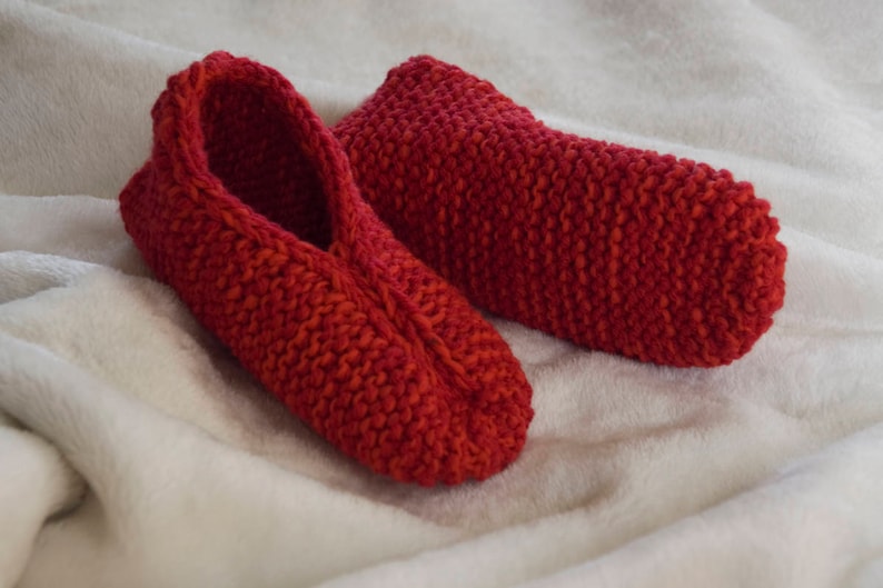 May include: A pair of red knitted slippers. The slippers are made with a soft, cozy yarn and have a simple, classic design.