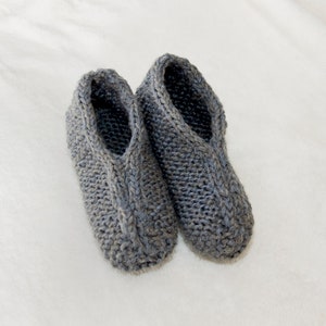 May include: A pair of gray knitted slippers. The slippers are made of a soft, cozy material and have a simple, classic design.
