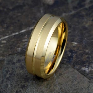 Gold tungsten 8mm ring tilted displaying brushed bands separated by polished groove accent and TUNGSTEN CARBIDE interior engraving, mens wedding band on stone