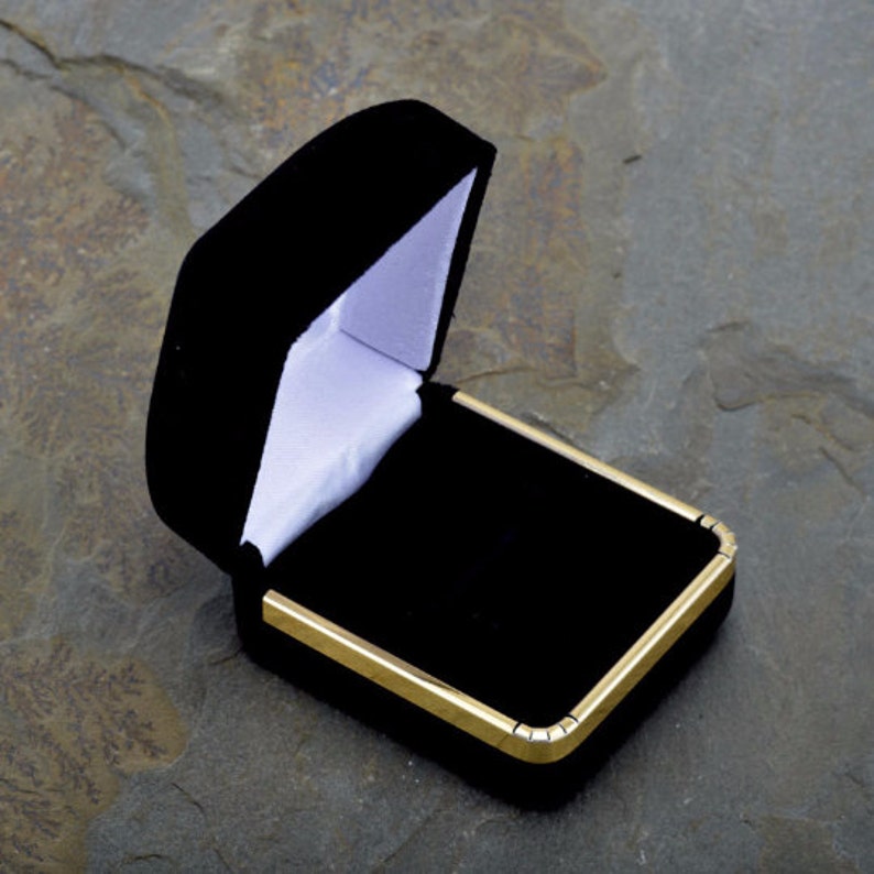 May include: A black velvet ring box with a gold trim. The box is open and the inside is lined with white velvet.