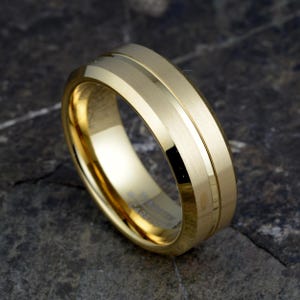 Gold tungsten 8mm mens band tilted displaying brushed finish with polished center groove accent and interior engraving space, wedding ring on concrete