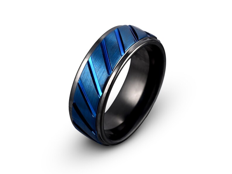 May include: A black and blue tungsten carbide ring with a grooved design. The ring has a brushed finish and a beveled edge.